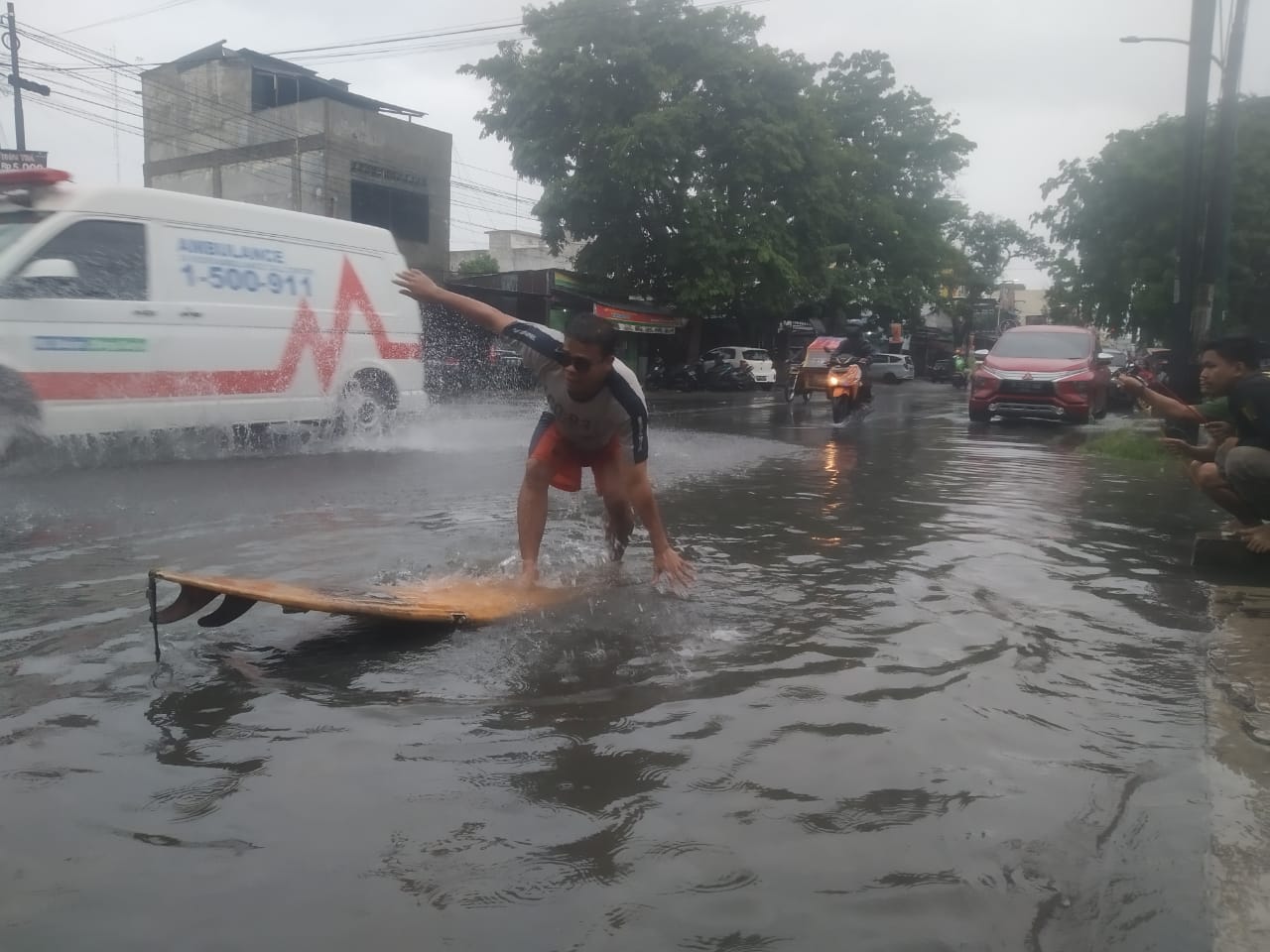 Foto-Seorang pemuda sedang berselancar di Jalan HM Joni, sedangkan dua rekannya memancing ikan. Diguyur Hujan Deras, Warga Medan Berselancar di Jalan Raya 1